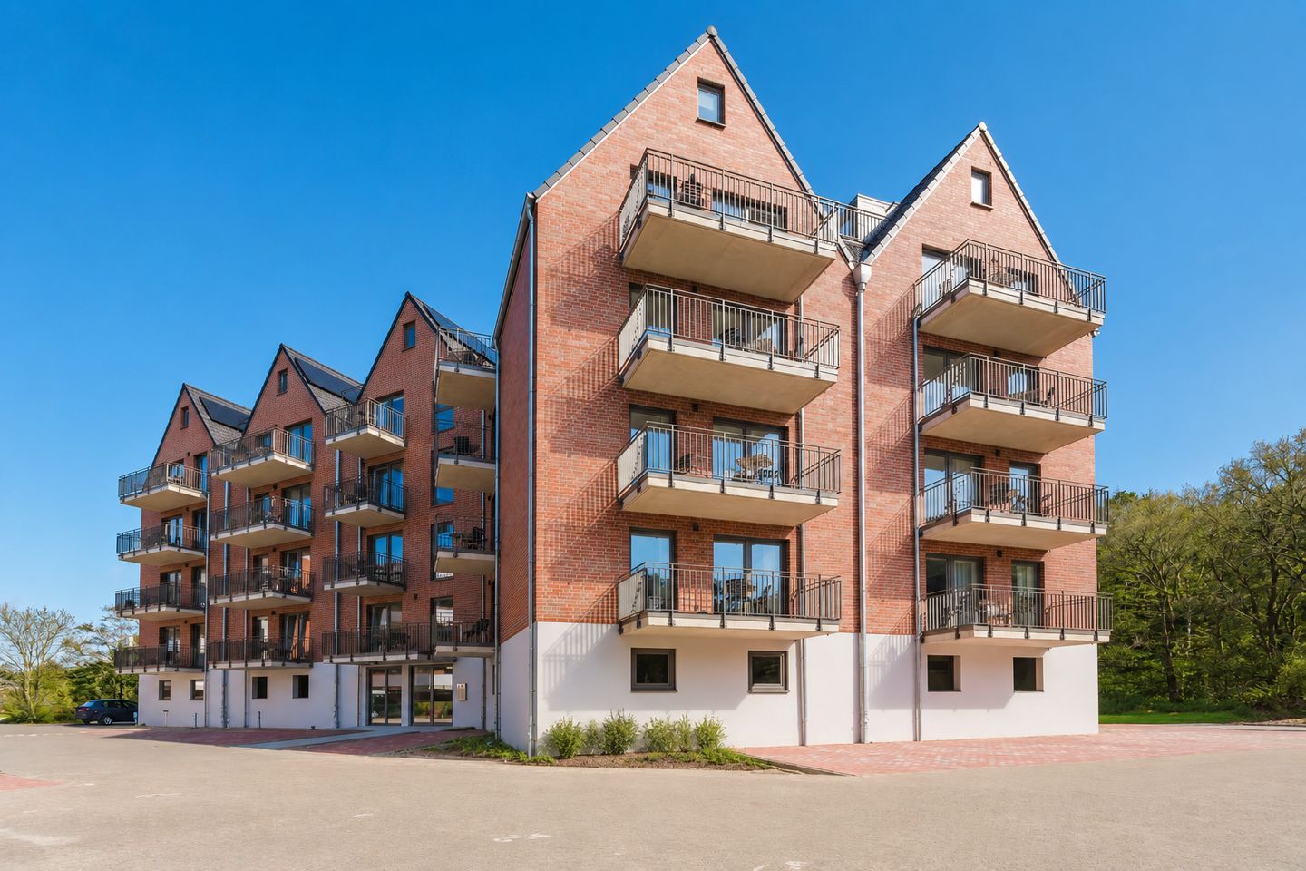 Ein mehrgeschossiges Wohngebäude mit Balkonen, einer flachen Dachterrasse und blauem Himmel.