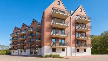 Ein mehrgeschossiges Wohngebäude mit Balkonen, einer flachen Dachterrasse und blauem Himmel.