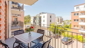 A balcony with a table and chairs, a flower vase, and a view of surrounding buildings. - MEERholung Vacation Rental 2.8 with Balcony, Just 400 m from the Sea - MEERholung House (Cuxhaven)