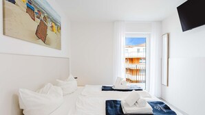 A hotel room with a bed, a painting, a TV, and a window with a view of buildings. - MEERholung Vacation Rental 2.8 with Balcony, Just 400 m from the Sea - MEERholung House (Cuxhaven)
