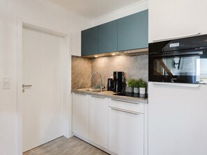 A compact kitchen with white cabinets, a black coffee maker, a stainless steel sink, and a built-in oven. - MEERholung Vacation Rental 4.9 – Stylish Penthouse Apartment with Access to a Rooftop Terrace - House (Cuxhaven)