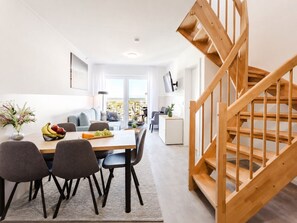 A modern interior with a dining area, a staircase, and a view of the outside. - MEERholung Vacation Rental 4.9 – Stylish Penthouse Apartment with Access to a Rooftop Terrace - House (Cuxhaven)