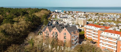 A coastal residential area with modern apartment buildings, a beach in the background, and a dense forested area.