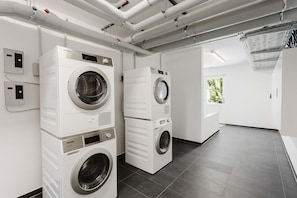 A modern laundry facility with stacked washers and dryers, a control panel, and a view of the outdoors. - MEERholung Vacation Rental 4.9 – Stylish Penthouse Apartment with Access to a Rooftop Terrace - House (Cuxhaven)