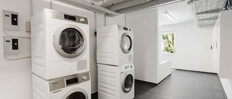 A modern laundry facility with stacked washers and dryers, a control panel, and a view of the outdoors.