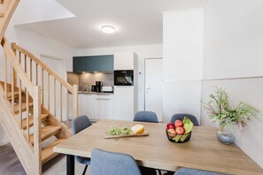 A modern kitchen with white cabinets, a wooden staircase, and a dining area with a table set for two. - MEERholung Vacation Rental 4.9 – Stylish Penthouse Apartment with Access to a Rooftop Terrace - House (Cuxhaven)