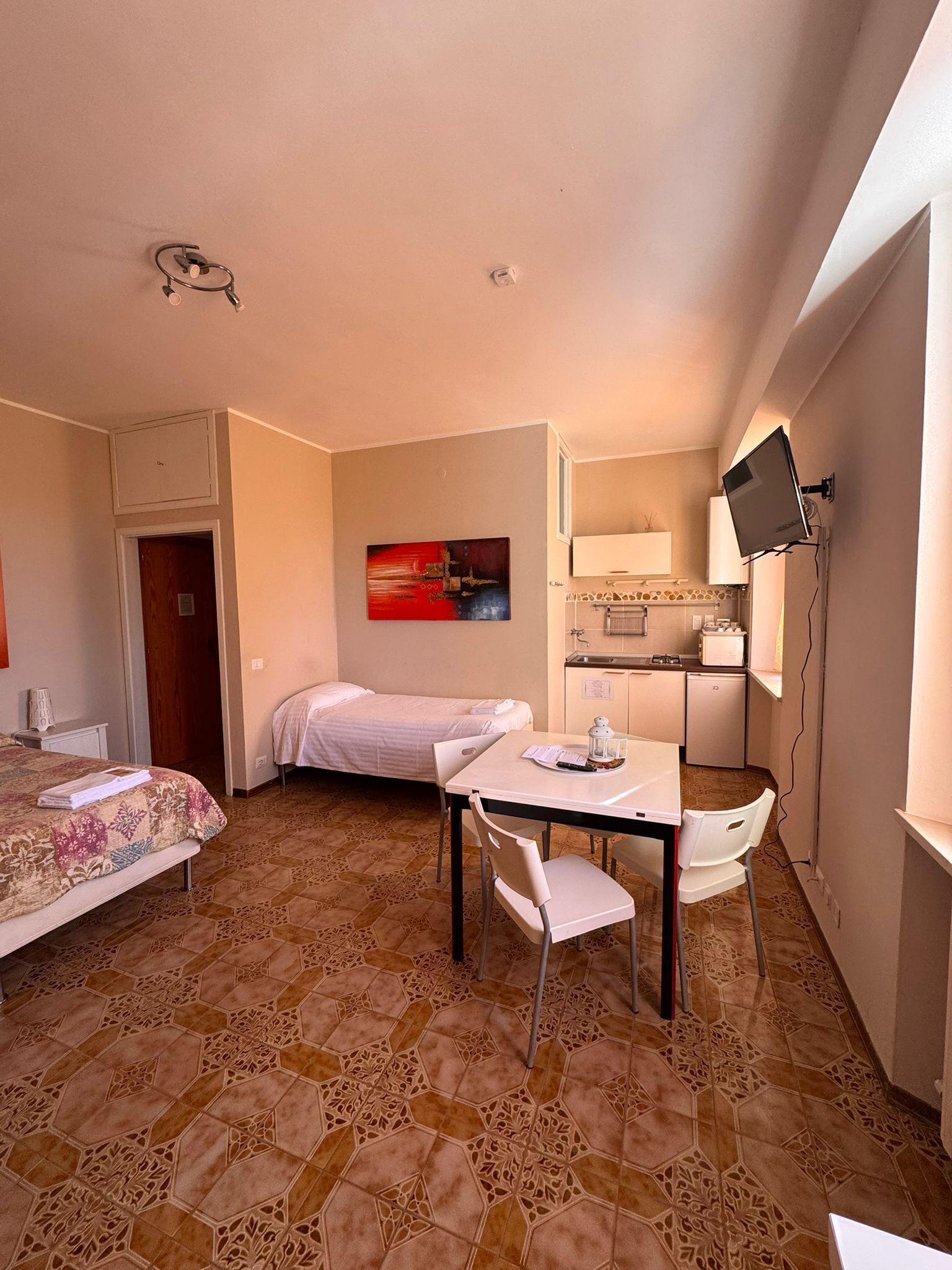 A hotel room with a bed, a desk with a chair, a television mounted on the wall, and a painting on the wall.