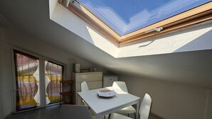 A modern room with a skylight, a dining table with chairs, a small kitchenette, and a sliding glass door. - 1.5 km from the AOI airport, comfortable studio apartments for your needs. (Falconara Marittima)