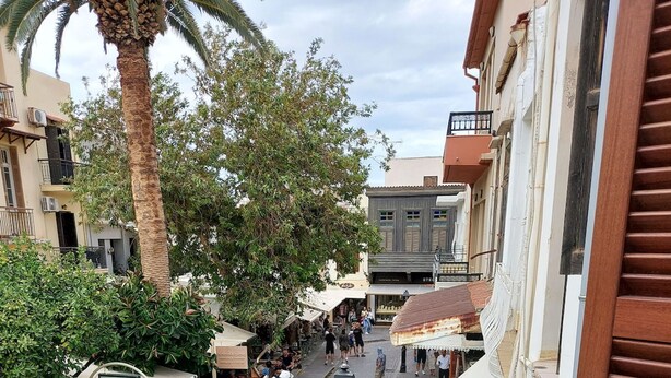A cobblestone street with outdoor seating, palm trees, and buildings with balconies. - Platanos Studio - Old Town Rethymno (Rethymno)