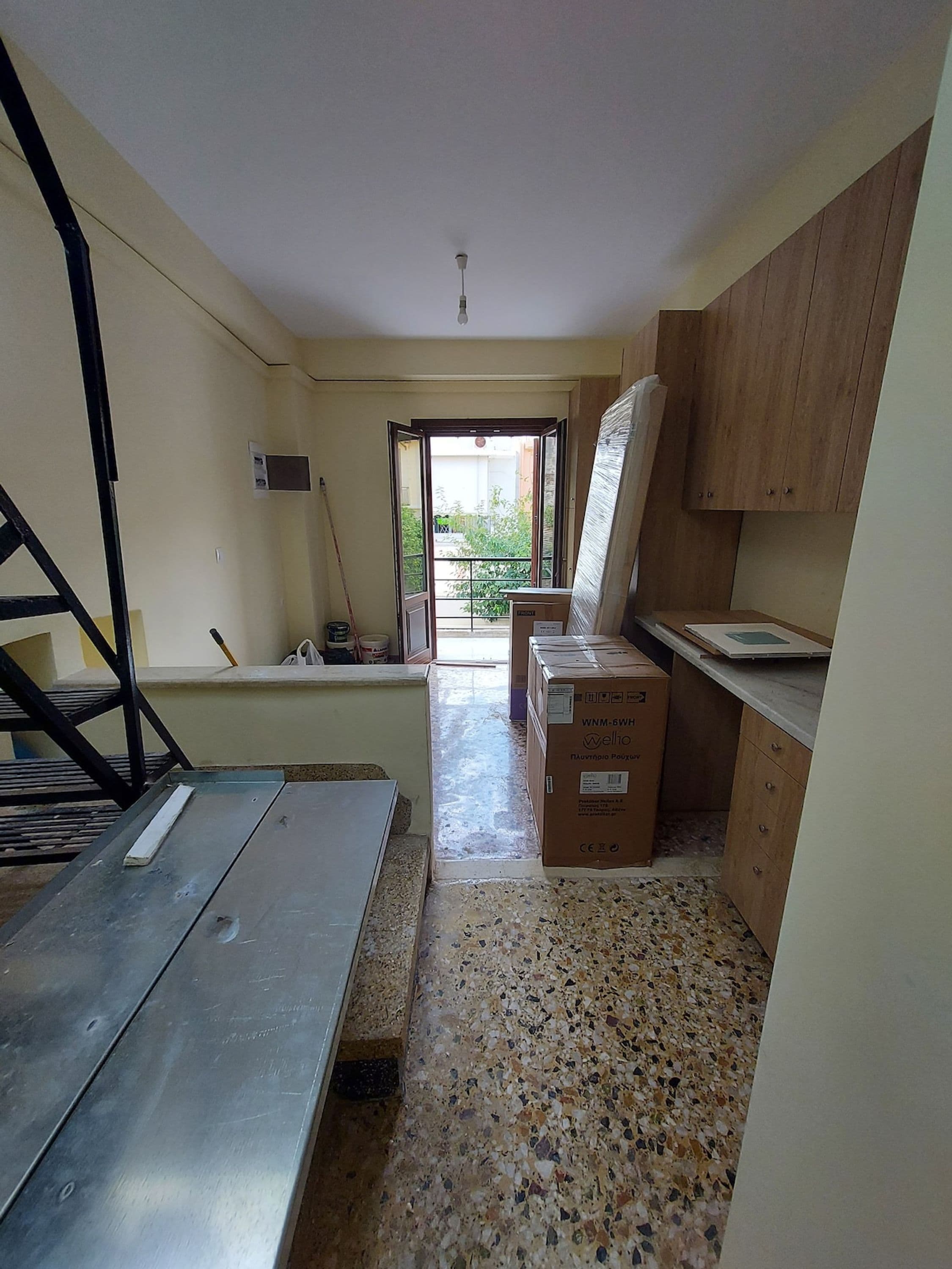 Quarto com cozinha compacta, porta para o exterior e mesa de metal.