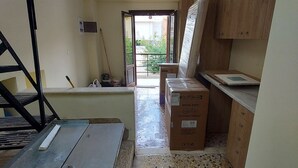 A room with a kitchenette, a door leading outside, and a metal table. - Platanos Studio - Old Town Rethymno (Rethymno)
