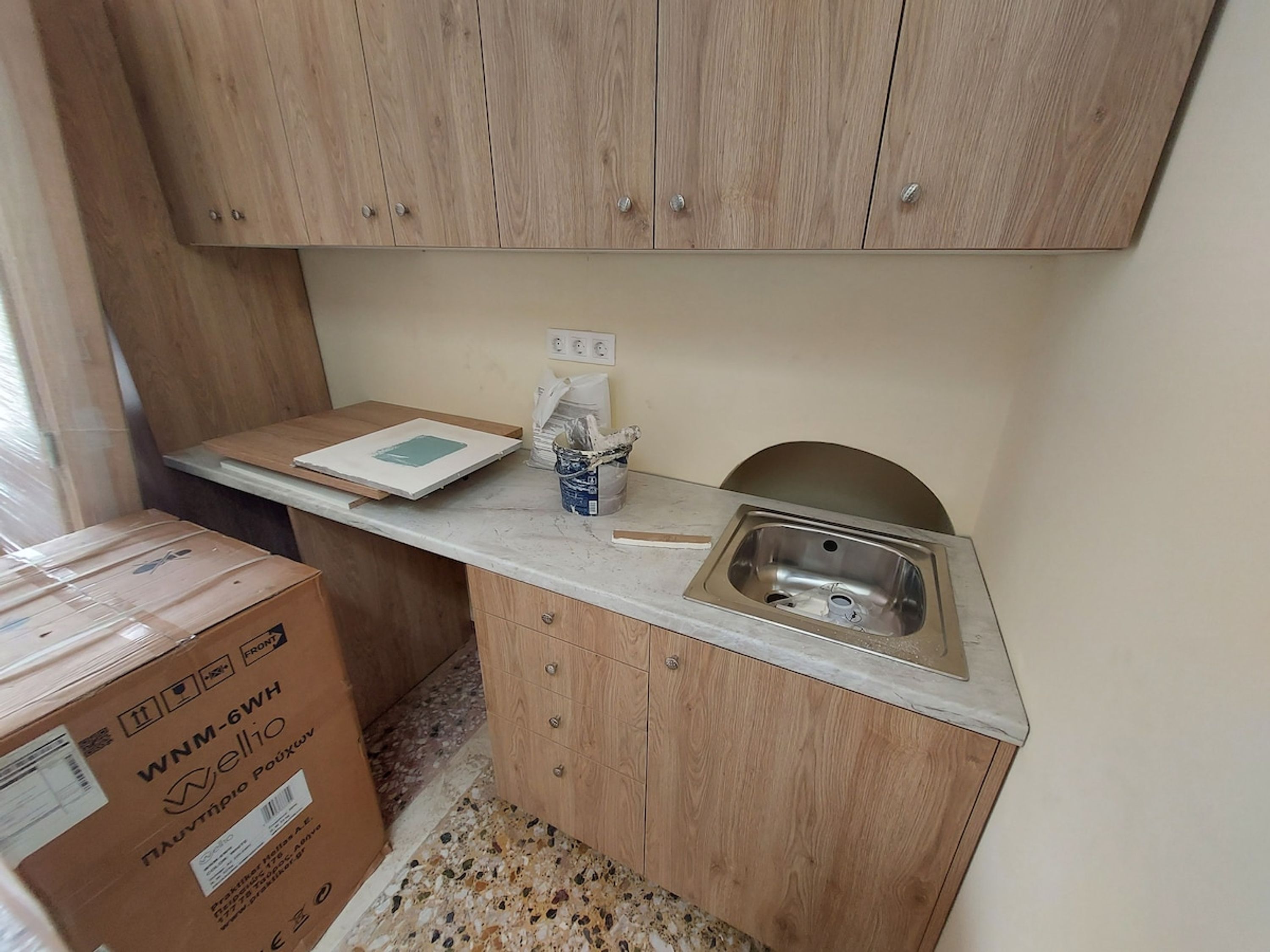 Une petite cuisine avec des armoires en bois, un plan de travail, un évier et une boîte étiquetée « WNM-6WH ».