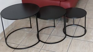 Un canapé en cuir rouge et trois tables rondes noires avec des pieds en métal.