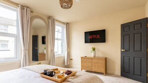 Un dormitorio con cama, una bandeja de desayuno, cómoda, televisor y puerta.