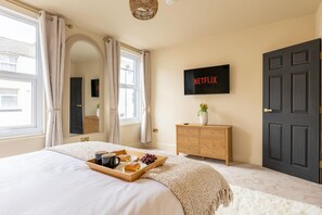 Ein Schlafzimmer mit Bett, einem Frühstücksbrett, einem Schminktisch, einem Fernseher und einer Tür.