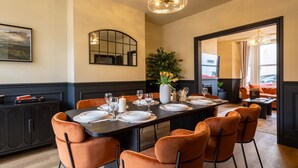Un comedor con una mesa larga dispuesta para seis personas, rodeada por seis sillas naranjas, un armario negro y un espejo en la pared.