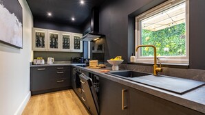 Una cocina moderna con armarios oscuros, encimera de madera, horno empotrado y ventana con vistas a zonas verdes.