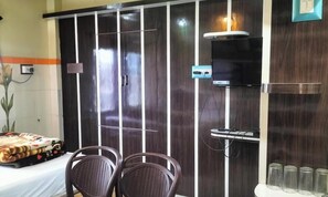 A room with a wardrobe, a television, a table with chairs, and a plant.