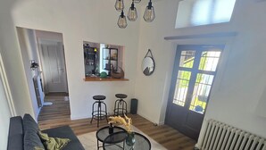 A living room with a sofa, coffee table, and a dining area with chairs. There is a kitchen visible in the background. - The Little House on the River (Castel Dè Ratti)