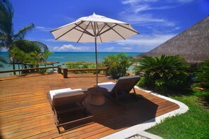 A wooden deck with lounge chairs and a table, overlooking a clear blue sea and palm trees. - Pitinga Hotel Pousada (Guesthouse) (Arraial D'Ajuda - Porto Seguro)