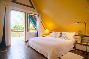 A bedroom with a bed, a nightstand, a lamp, and a view of a balcony. - Pitinga Hotel Pousada (Guesthouse) (Arraial D'Ajuda - Porto Seguro)