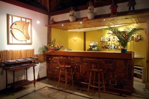 A bar area with a wooden counter, stools, and a decorative wall with a fish design. - Pitinga Hotel Pousada (Guesthouse) (Arraial D'Ajuda - Porto Seguro)
