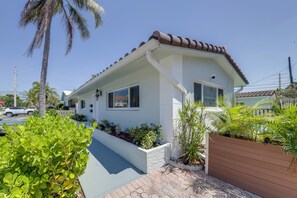 Ein einstöckiges Haus mit einem Ziegeldach, einer Veranda und einem kleinen Garten mit verschiedenen Pflanzen.