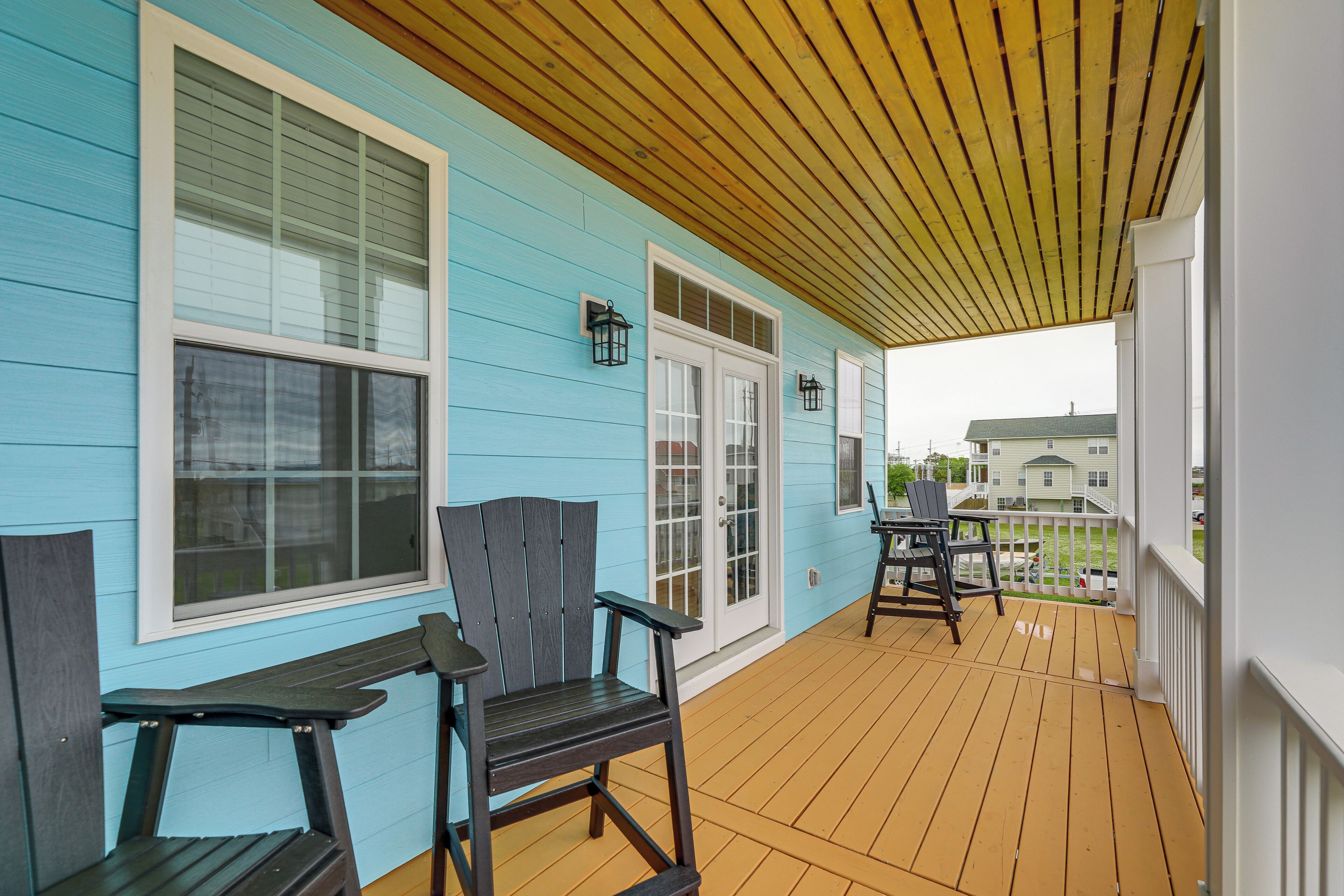A covered porch with two chairs and a table, a wooden ceiling, and a house with blue siding and white trim.