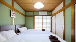 Une chambre d’hôtel avec deux lits, un plafond en bois, une fenêtre avec des panneaux coulissants de style japonais (shoji) et un appareil de climatisation.