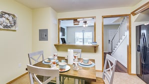 Un coin repas avec une table en bois dressée pour quatre personnes, entourée de chaises blanches. Un miroir est accroché au mur au-dessus de la table et reflète la pièce.