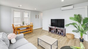 Ein Wohnzimmer mit einer Couch, einem Couchtisch, einem Fernseher auf einem Schrank, einem Esstisch mit Stühlen und einer Zimmerpflanze.