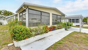 A single-story house with a large window, a covered porch, and a garden with various plants and flowers. - Bonita Beach 7 Mi: 55+ Community w/ Pool Access (Bonita Springs)