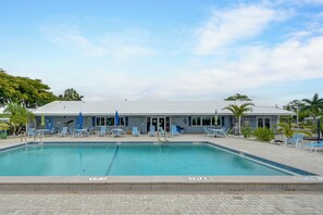 Ein Pool mit Liegestühlen und Sonnenschirmen, ein Gebäude mit flachem Dach sowie Palmen.