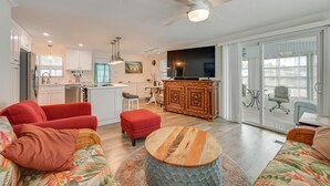 A modern living room with a sofa, ottoman, and coffee table, a kitchen with white cabinets, and a dining area with a table and chairs. - Bonita Beach 7 Mi: 55+ Community w/ Pool Access (Bonita Springs)