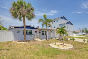 A two-story house with a blue roof, a fenced yard, and palm trees. - Canal-Front Oasis in Hudson: Patio + Private Dock! (Hudson)