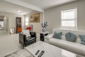 A living room with a white sofa, a black leather chair, a marble coffee table, and a small side table with a vase of flowers.