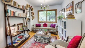 Een gezellige woonkamer met een boekenkast, een bank, een salontafel en een groot raam.