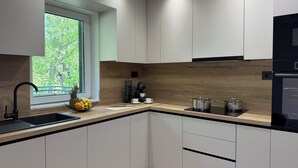 A modern kitchen with white cabinets, a wooden backsplash, and a window with a view of greenery. - Sunset luxury apartment (Tučepi)