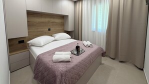 A modern bedroom with a wooden headboard, a large bed with a pink quilt, two white pillows, a glass of water, and neatly folded towels. - Sunset luxury apartment (Tučepi)