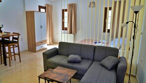 A living room with a sofa, a small table, a wardrobe, and a bed with curtains. - Gefyra Studios Filoti Naxos (Naxos)