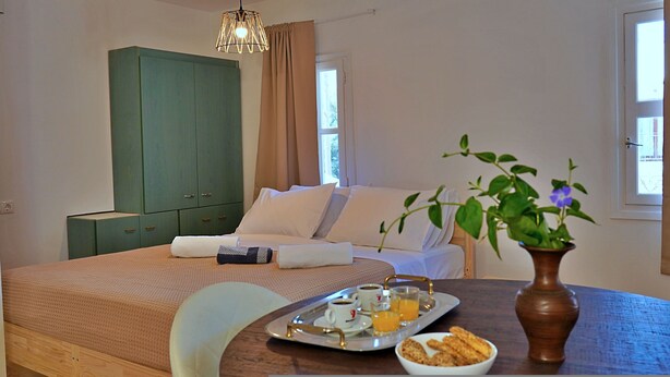 Une chambre d’hôtel avec un lit, une armoire verte, une table à manger avec des aliments pour le petit-déjeuner et une fenêtre avec des rideaux.