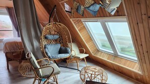 A cozy room with a sloped ceiling, wicker furniture, and a large window. - Bernardlhermite (La Hague)