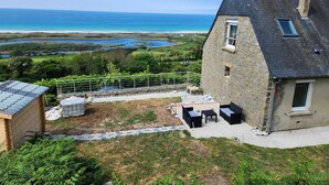 A stone house with a patio and outdoor seating area overlooking a coastal landscape. - Bernardlhermite (La Hague)