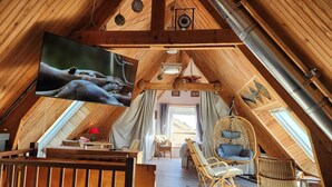 An attic room with a TV, wooden beams, a hanging chair, and a bed. - Bernardlhermite (La Hague)