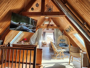 Ein Dachzimmer mit Fernseher, Holzbalken, einem Hängesessel und einem Bett.