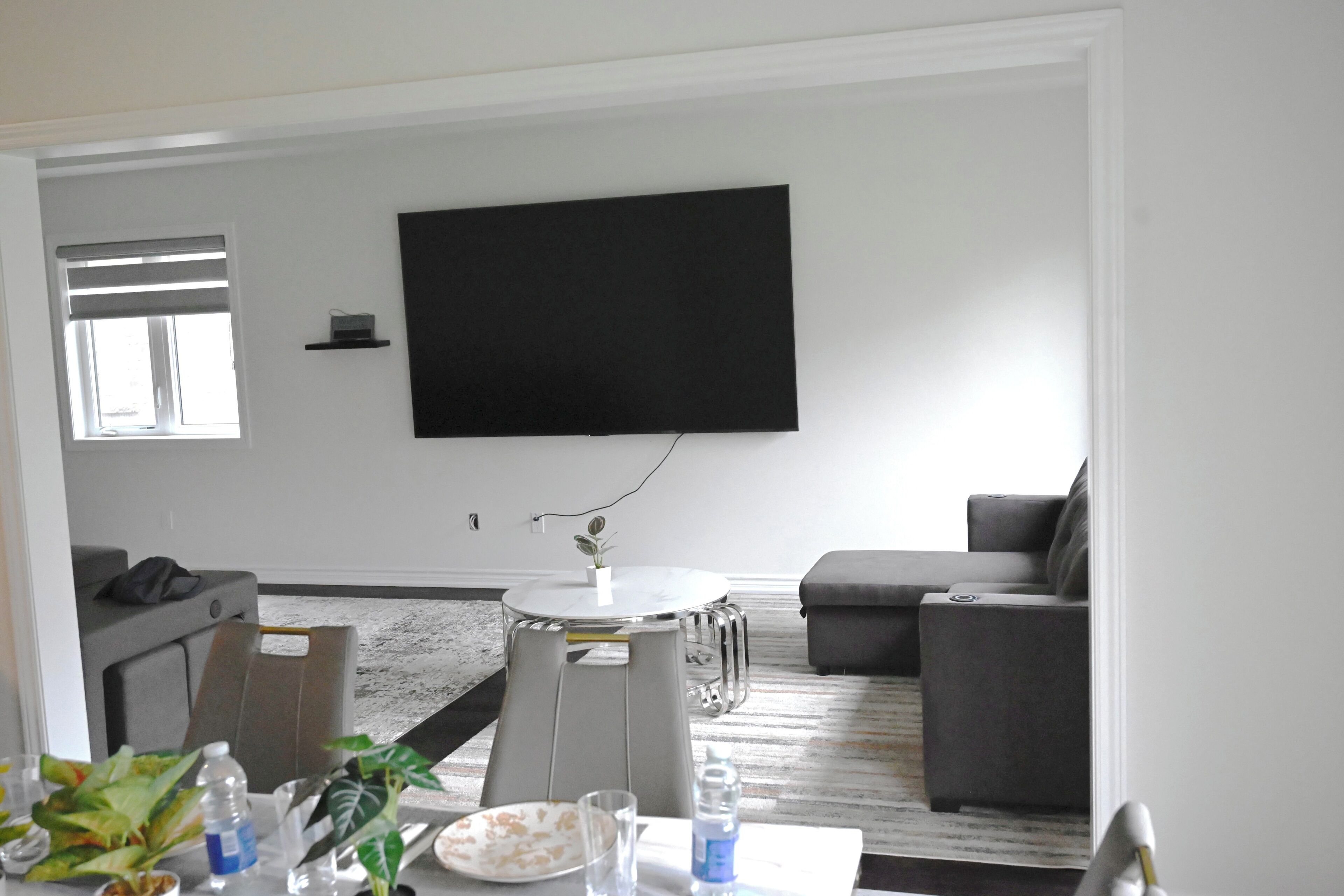 Ein Wohnzimmer mit Flachbildfernseher, grauen Sofas, einem Couchtisch und einem Esstisch mit Stühlen.