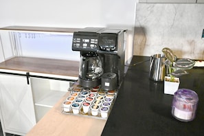 A coffee machine with a coffee pod holder, a stainless steel pitcher, and a small potted plant on a kitchen counter.