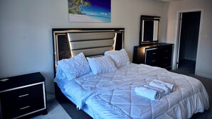 A neatly made bed with a headboard, a bedside table, a dresser, and a painting on the wall. - Elegant 4-Bedroom Luxury Retreat with 2 Sofa Beds, Close to Niagara Falls (Thorold)
