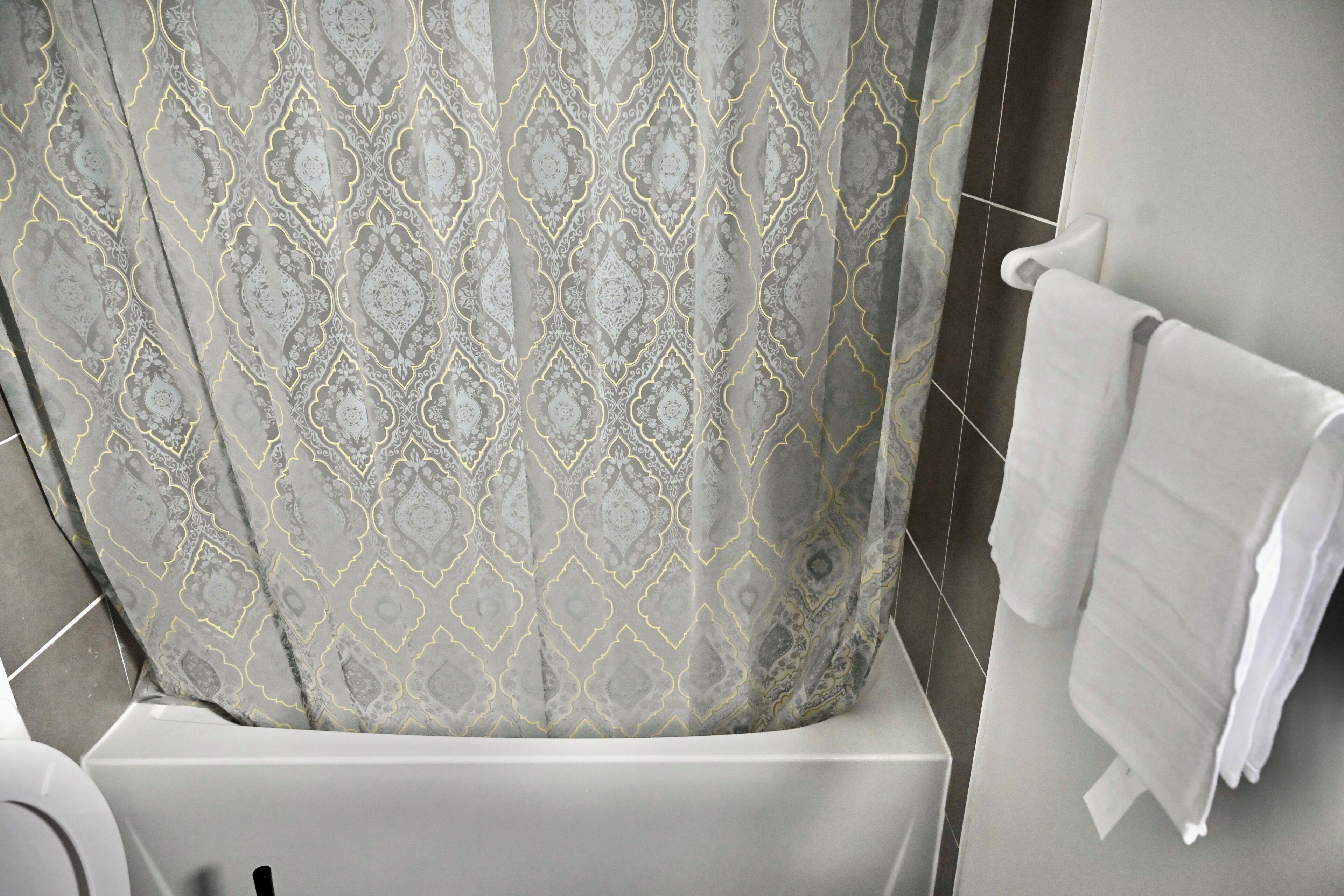 Een badkamer met een gordijn met patroon, een witte badkuip en een handdoekhouder.