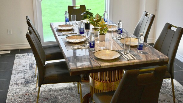 A dining table set with plates, cutlery, and water bottles, surrounded by chairs, with a view of a green lawn through a window. - Elegant 4-Bedroom Luxury Retreat with 2 Sofa Beds, Close to Niagara Falls (Thorold)